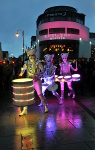 Spark! street drumming performers illumiated in multicolour lights outside The Brewery Quarter